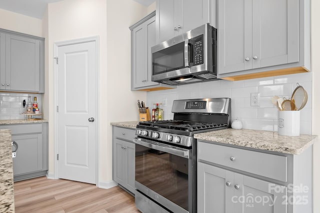 kitchen featuring light stone counters, appliances with stainless steel finishes, gray cabinets, and light wood-type flooring