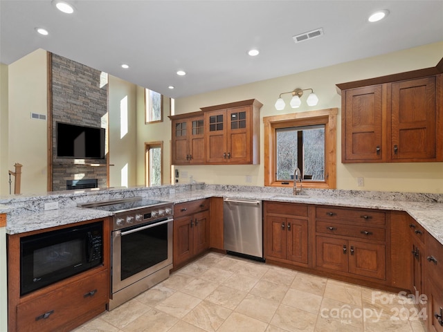 kitchen with kitchen peninsula, appliances with stainless steel finishes, light stone counters, sink, and a stone fireplace