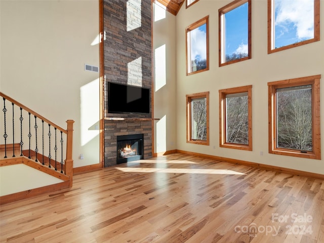 unfurnished living room with light hardwood / wood-style floors, a stone fireplace, and a towering ceiling