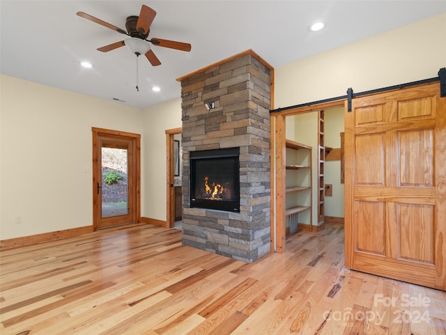 unfurnished living room featuring ceiling fan, a stone fireplace, and light wood-type flooring