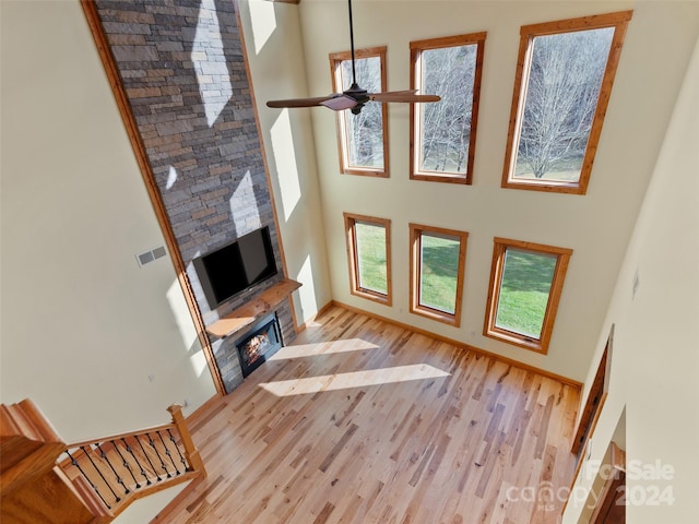 unfurnished living room featuring a stone fireplace, ceiling fan, light hardwood / wood-style flooring, and a towering ceiling