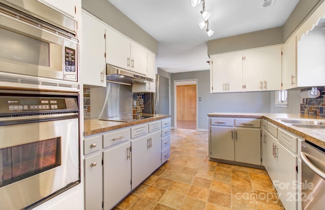 kitchen featuring decorative backsplash, track lighting, stainless steel appliances, sink, and white cabinets