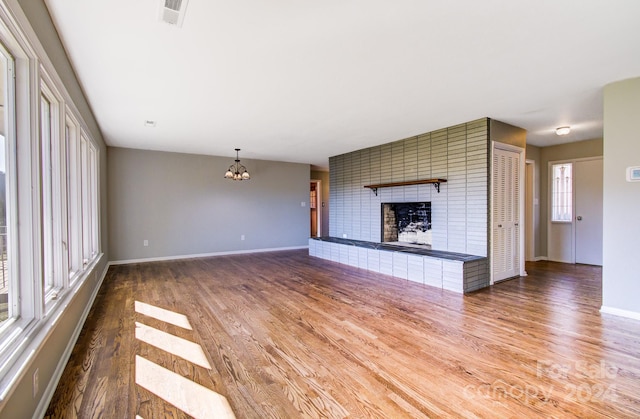 unfurnished living room with hardwood / wood-style flooring, a brick fireplace, and an inviting chandelier