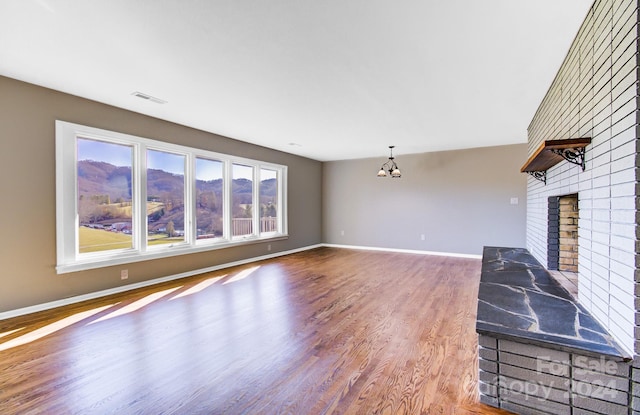 unfurnished living room with an inviting chandelier, wood-type flooring, and a brick fireplace