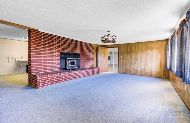 unfurnished living room featuring carpet flooring, a wood stove, wood walls, and a textured ceiling