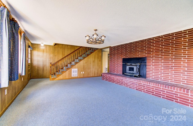 unfurnished living room featuring a wood stove, carpet floors, a chandelier, a textured ceiling, and wooden walls