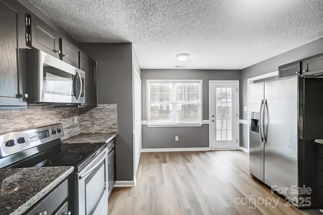 kitchen with dark stone countertops, a textured ceiling, decorative backsplash, appliances with stainless steel finishes, and light wood-type flooring