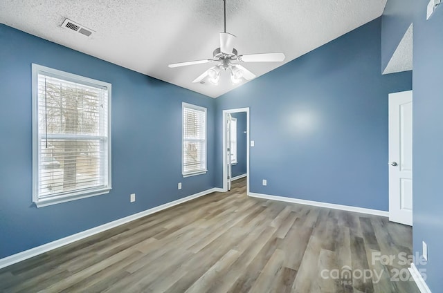 spare room with a textured ceiling, light hardwood / wood-style floors, vaulted ceiling, and ceiling fan