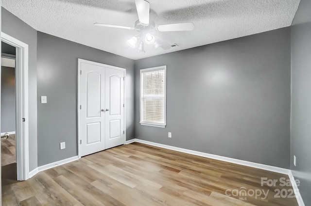 unfurnished bedroom featuring ceiling fan, a closet, a textured ceiling, and light wood-type flooring