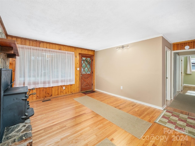 foyer entrance featuring a wood stove, hardwood / wood-style floors, a textured ceiling, wooden walls, and ornamental molding