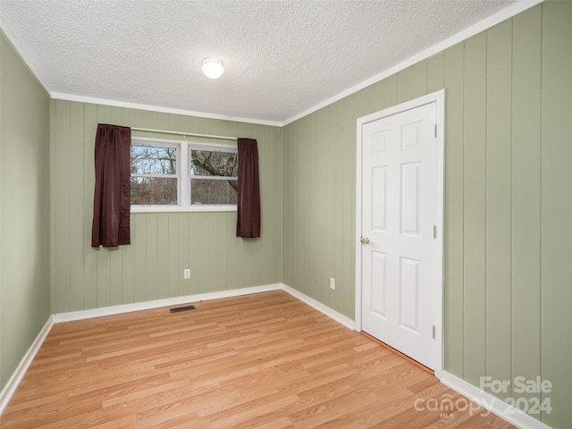 empty room featuring wood walls, light hardwood / wood-style flooring, and crown molding