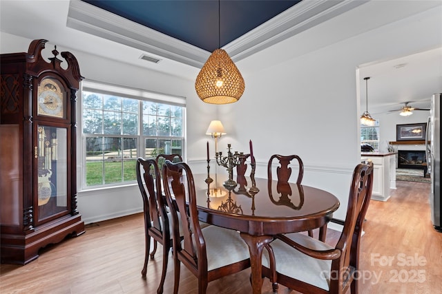 dining room featuring a raised ceiling, ceiling fan, crown molding, and light wood-type flooring