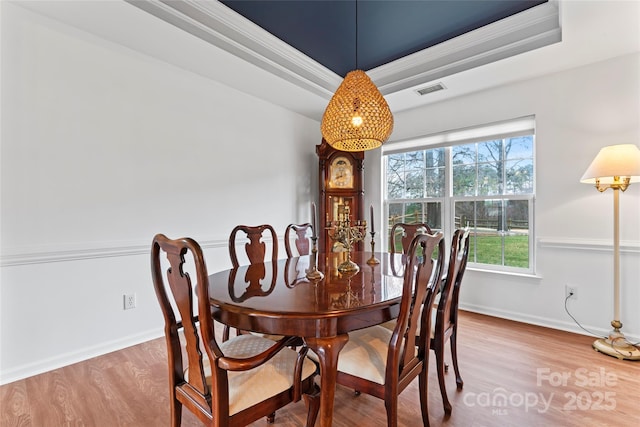 dining room with a raised ceiling, wood-type flooring, and ornamental molding