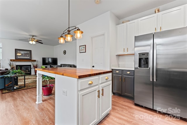 kitchen with wooden counters, a brick fireplace, stainless steel fridge, decorative light fixtures, and white cabinetry