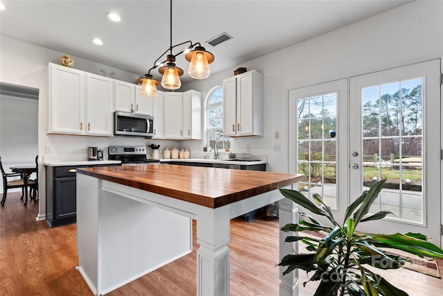 kitchen featuring butcher block counters, white cabinetry, stainless steel appliances, light hardwood / wood-style floors, and decorative light fixtures