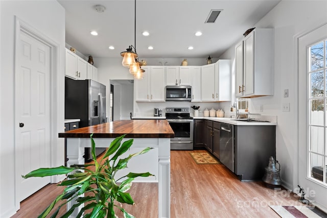 kitchen featuring appliances with stainless steel finishes, a kitchen island, butcher block countertops, white cabinetry, and hanging light fixtures