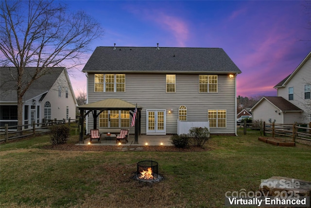 back house at dusk featuring a gazebo, an outdoor fire pit, a patio area, and a lawn