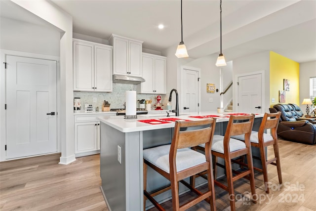 kitchen featuring a breakfast bar, a center island with sink, sink, decorative light fixtures, and white cabinetry