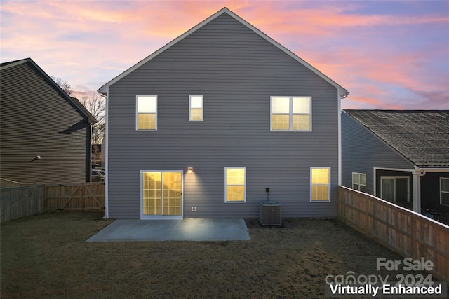 back house at dusk with a patio area, a yard, and cooling unit