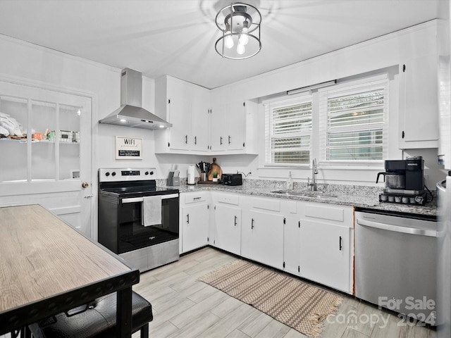 kitchen featuring light wood-type flooring, stainless steel appliances, sink, wall chimney range hood, and white cabinetry