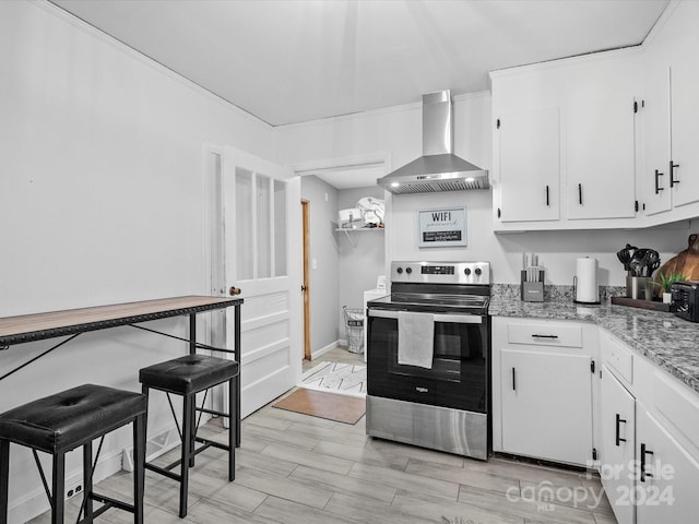 kitchen featuring stainless steel range with electric stovetop, wall chimney range hood, light wood-type flooring, light stone counters, and white cabinetry