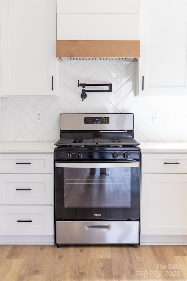 kitchen with stainless steel gas range oven, light wood-type flooring, premium range hood, white cabinets, and light countertops