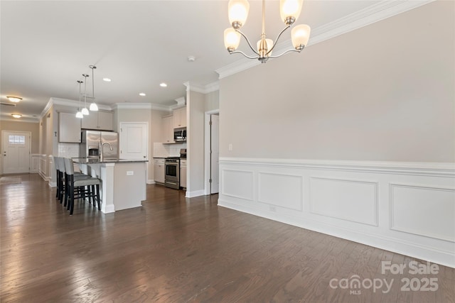 kitchen featuring a notable chandelier, pendant lighting, a center island with sink, appliances with stainless steel finishes, and ornamental molding