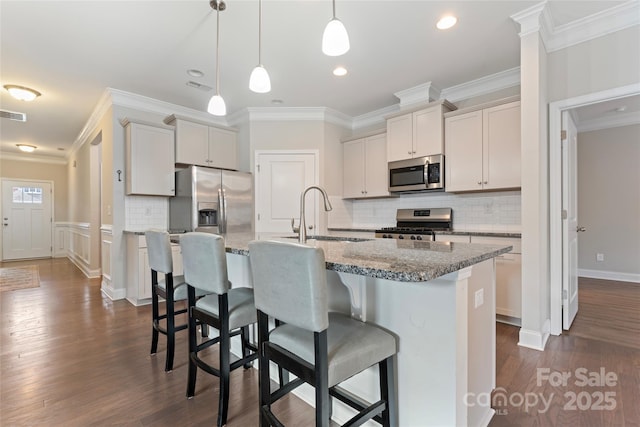 kitchen with hanging light fixtures, stainless steel appliances, a kitchen island with sink, and sink