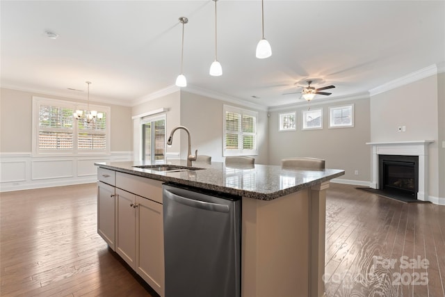 kitchen featuring dishwasher, a kitchen island with sink, sink, dark stone countertops, and ornamental molding