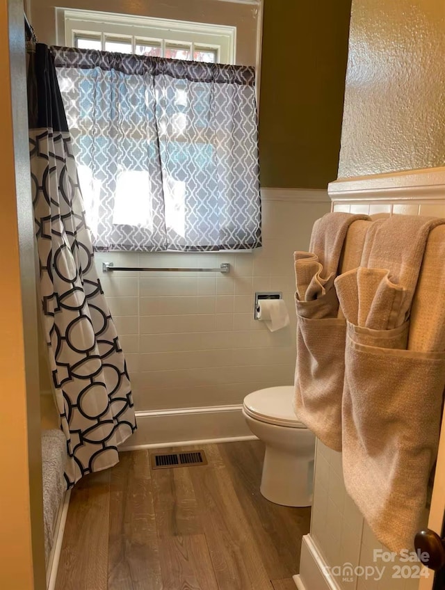 bathroom with hardwood / wood-style flooring, toilet, and tile walls