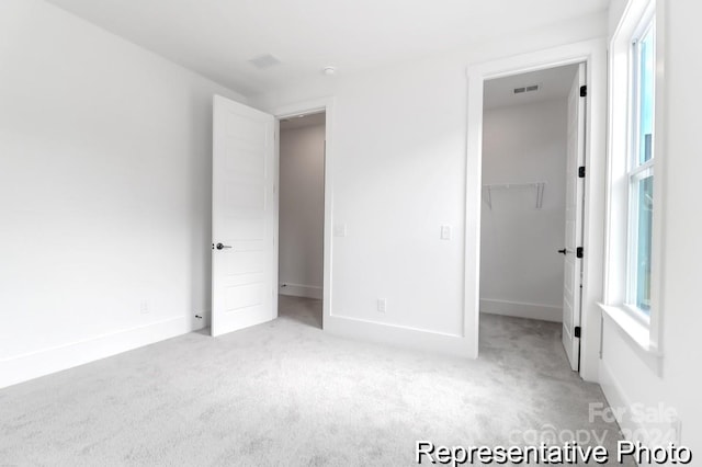 unfurnished bedroom with a walk in closet, a closet, and light colored carpet