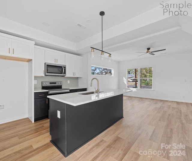 kitchen with appliances with stainless steel finishes, a kitchen island with sink, sink, decorative light fixtures, and white cabinetry