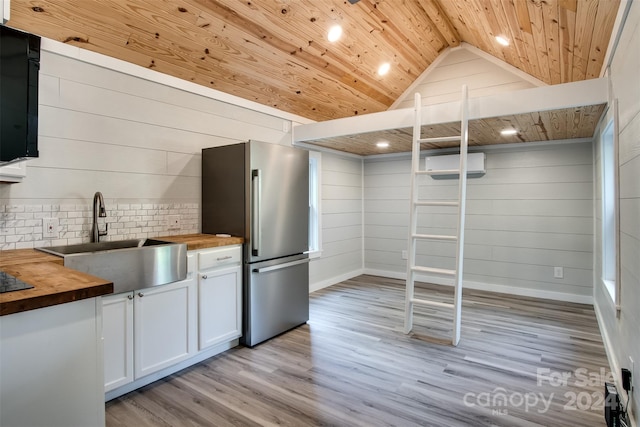 kitchen featuring wood counters, sink, light hardwood / wood-style floors, stainless steel refrigerator, and lofted ceiling