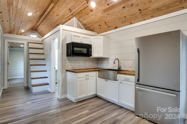 kitchen featuring wood counters, vaulted ceiling, sink, white cabinets, and stainless steel refrigerator