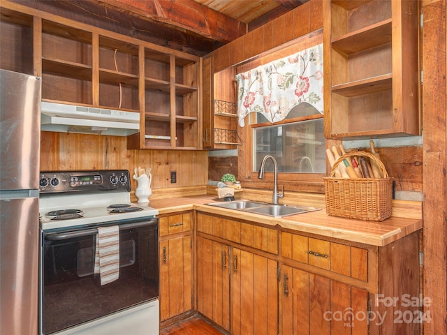 kitchen featuring stainless steel fridge, white electric range oven, sink, beamed ceiling, and wood walls