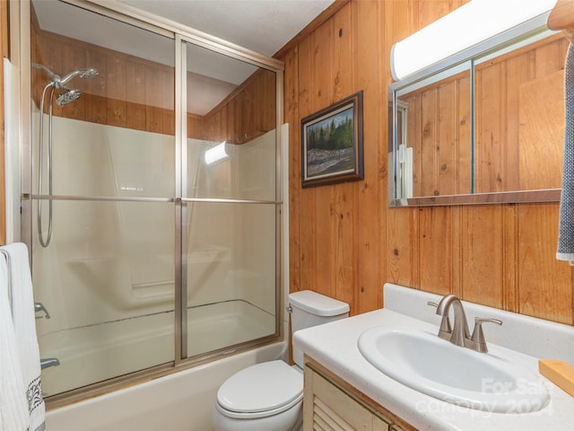 full bathroom featuring shower / bath combination with glass door, vanity, toilet, and wood walls