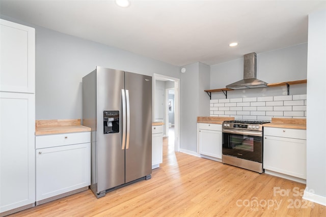 kitchen with stainless steel appliances, wall chimney range hood, wood counters, decorative backsplash, and white cabinets