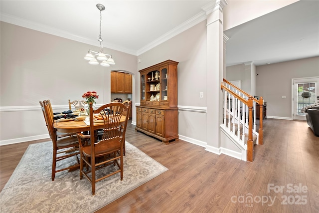 dining space featuring decorative columns, hardwood / wood-style flooring, ornamental molding, and a notable chandelier