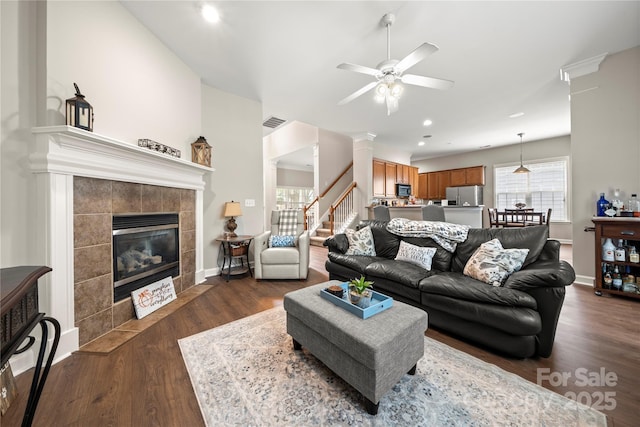 living room with ceiling fan, dark hardwood / wood-style flooring, a tile fireplace, and decorative columns