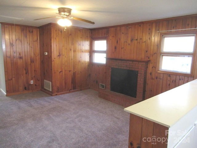 unfurnished living room featuring plenty of natural light, wood walls, ceiling fan, and a brick fireplace