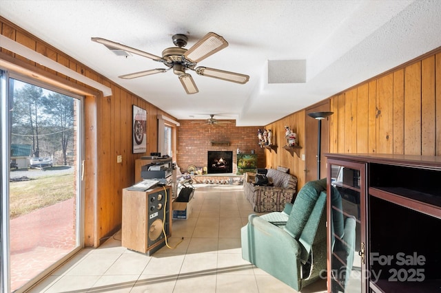 living room with brick wall, a textured ceiling, wooden walls, light tile patterned floors, and a fireplace