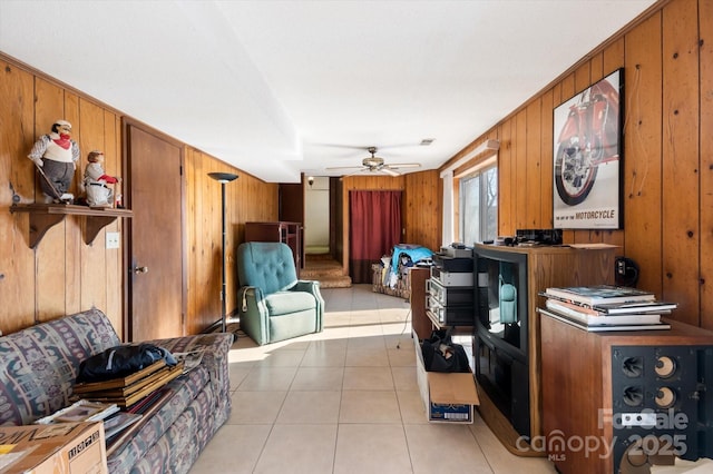 living room featuring ceiling fan, light tile patterned flooring, and wooden walls