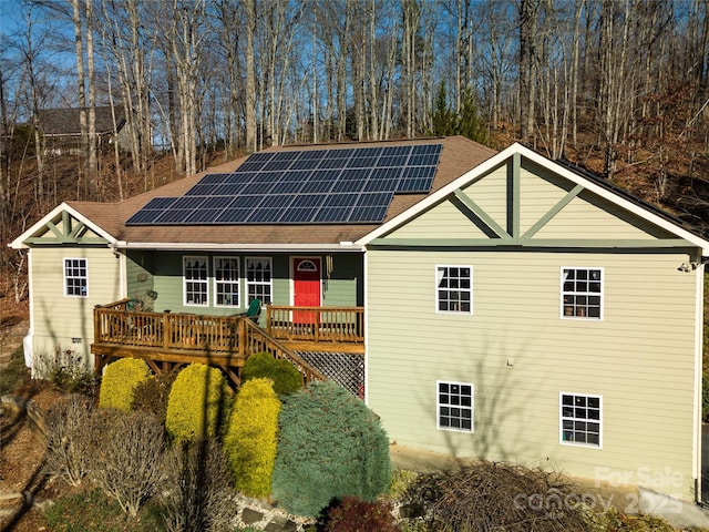 view of front facade with a wooden deck, roof with shingles, and solar panels