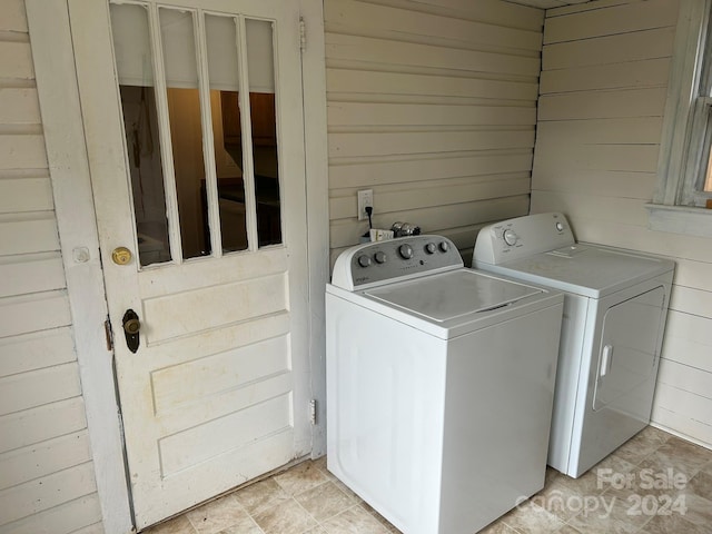 clothes washing area with washer and clothes dryer and wooden walls