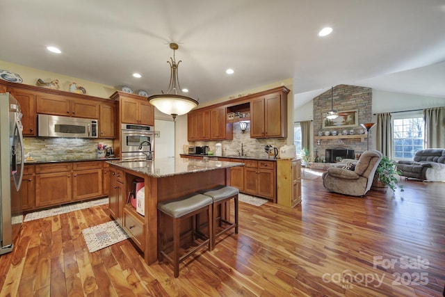 kitchen with lofted ceiling, a kitchen island with sink, hanging light fixtures, light stone countertops, and appliances with stainless steel finishes