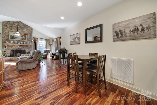 dining space with a stone fireplace, ceiling fan, dark hardwood / wood-style floors, and vaulted ceiling