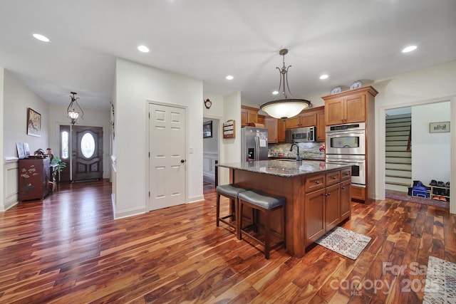 kitchen with dark wood-type flooring, an island with sink, hanging light fixtures, and appliances with stainless steel finishes