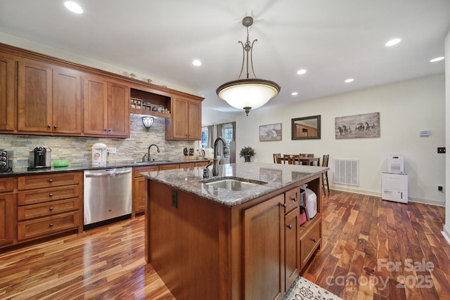 kitchen featuring sink, a center island with sink, dark stone countertops, dishwasher, and hanging light fixtures