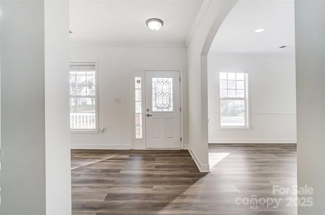 entryway featuring baseboards, ornamental molding, arched walkways, and dark wood-style flooring