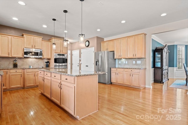 kitchen featuring stainless steel appliances, light stone counters, decorative light fixtures, a kitchen island, and light wood-type flooring